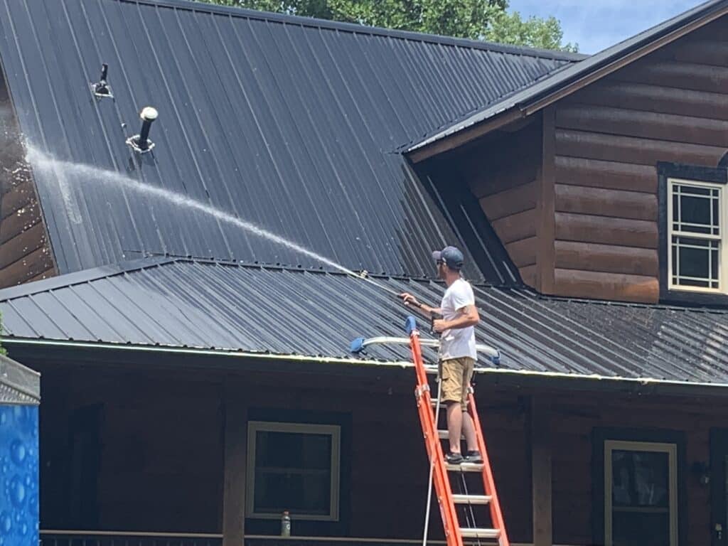 Technician performing safe metal roof cleaning using soft washing methods on a residential home in Asheboro NC