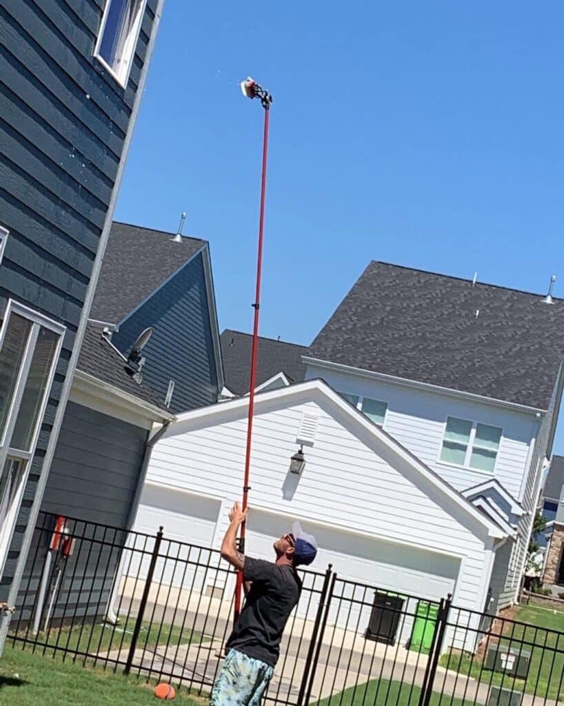 Technician cleaning exterior windows on a residential home using a purified water window cleaning system for spot-free results.